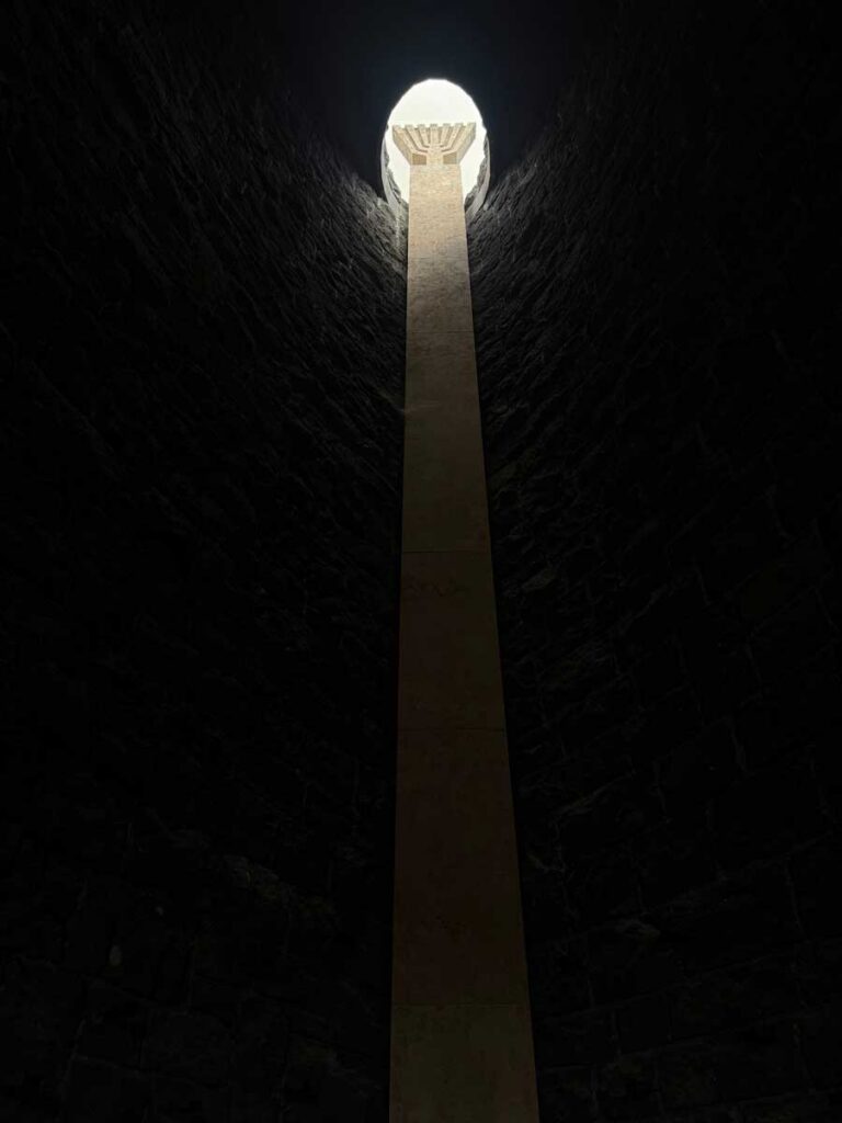 The design of the Jewish Memorial symbolizes the descent into the darkness of the Holocaust. At the lowest point, light streams in from an opening in the roof. The menorah symbolizes the survival and continuity of Jewish life past the murder of six million Jews.